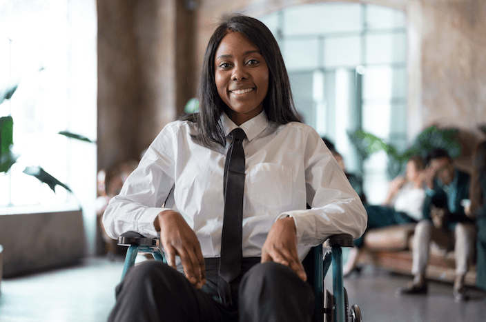 A confident professional woman in a white shirt and tie sits in a wheelchair, with a poised and cheerful demeanor, representing the empowerment that able accounts can offer.