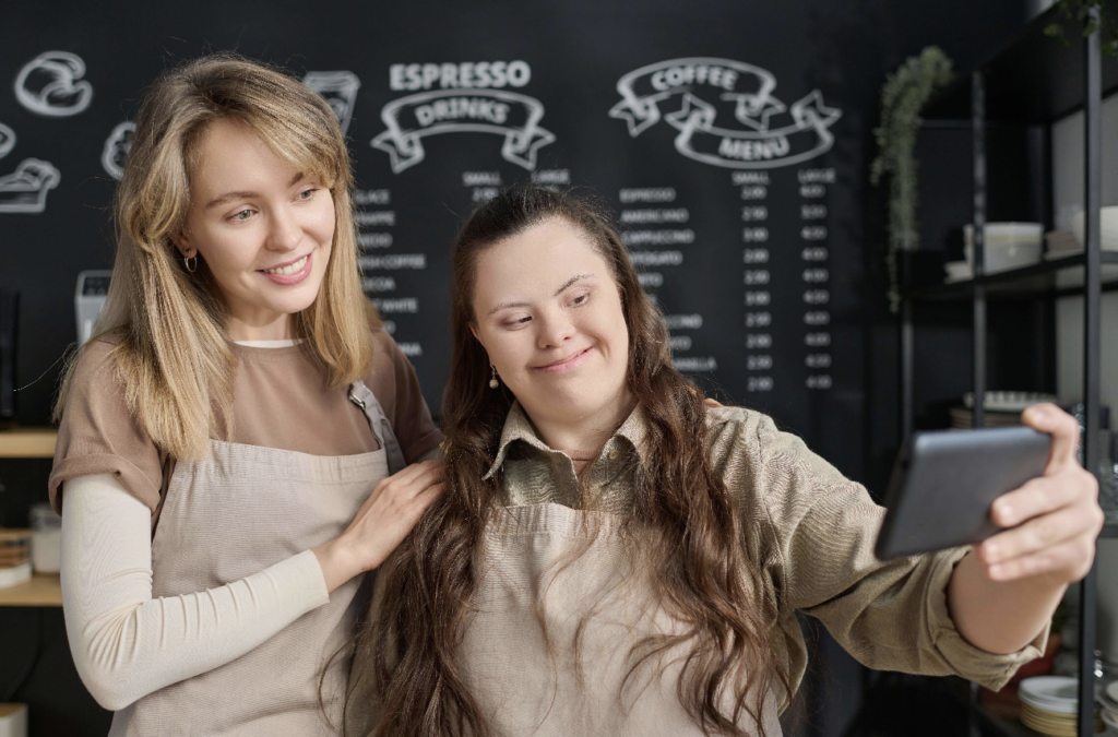 Two women in a cozy café setting, one with Down syndrome, take a selfie together, symbolizing the shared experiences and support facilitated by a first party special needs trust.