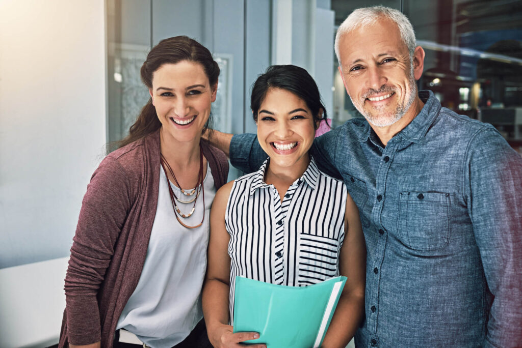 Three diverse professionals, smiling confidently in an office setting, which could represent the informed decision-making involved in choosing a health care proxy.