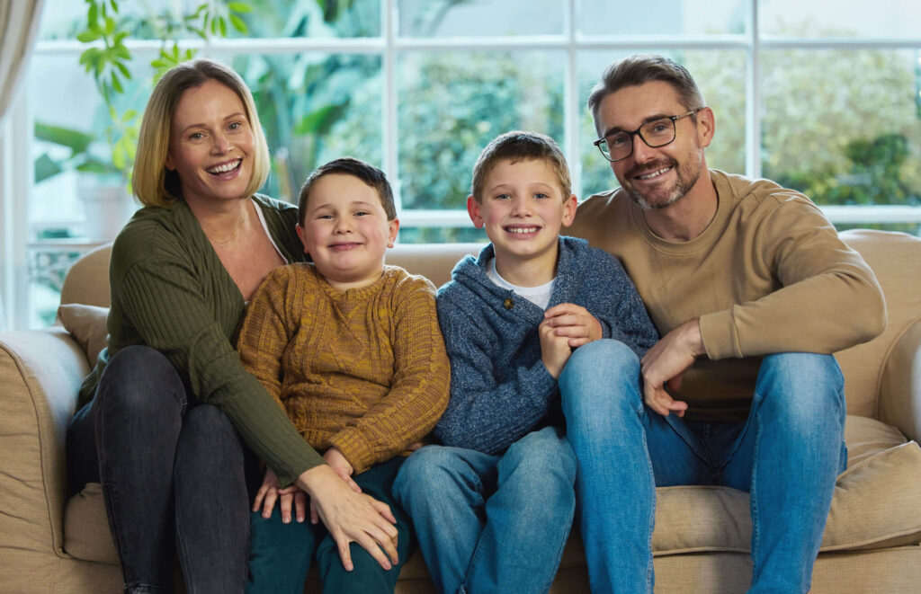 A family of four sits closely on a couch, smiling brightly, which represents the unity and forward-thinking approach of drafting a letter of intent for a family member with special needs.