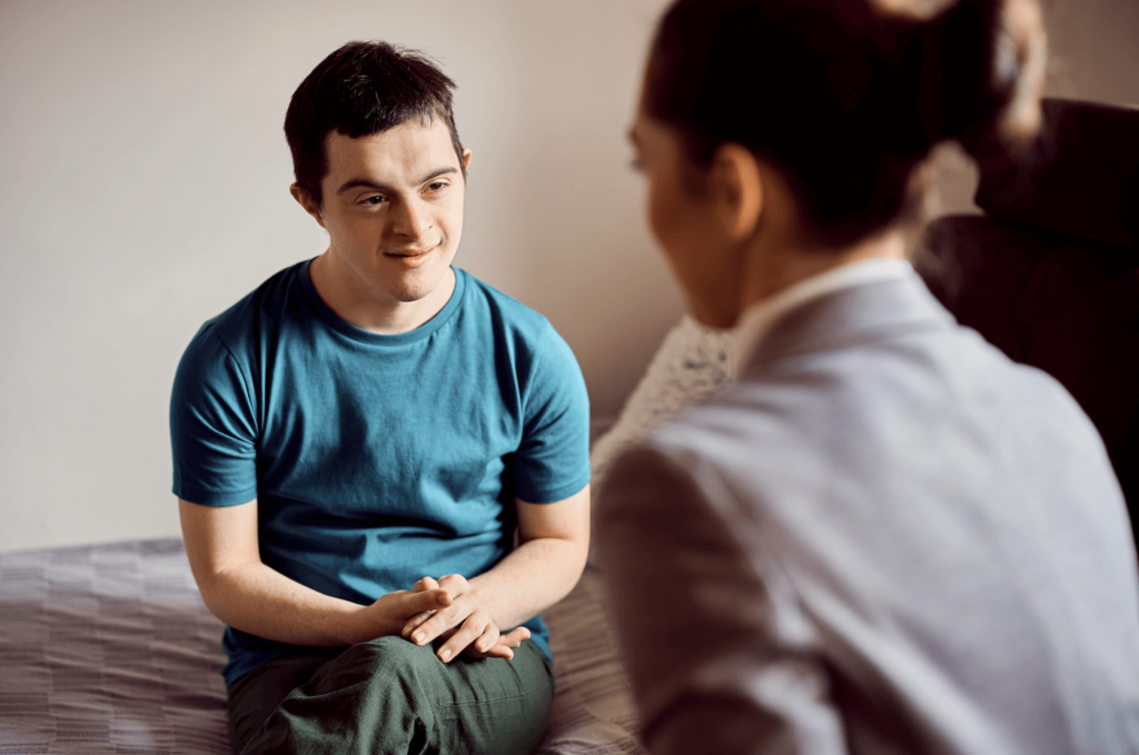 An adult with Down syndrome in a blue t-shirt sits comfortably, engaging in conversation with a person in a blurred foreground, symbolizing the discussion of power of attorney for education.