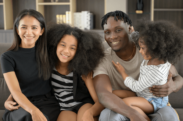 A joyful family of four with two children sitting on a couch, the warmth of their smiles reflecting the security and peace of mind a first party special needs trust can provide.