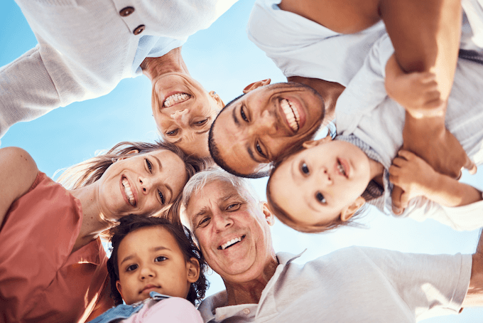 A multi-generational family forms a close circle from a low angle view, their faces beaming with happiness and unity, symbolizing the support provided by special needs trusts.