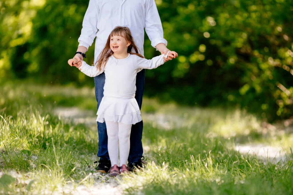 A joyful girl with special needs holds hands with an adult as they walk through a lush green park, symbolizing the support provided by special needs trusts.